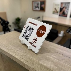QR a NFC stojan s vlastným logom umiestnený na recepčnom pulte, umožňujúci platbu QR kódom a rýchly prístup na Instagram.