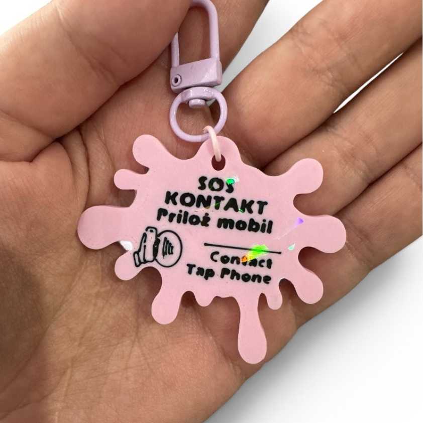 SOS NFC kľúčenka pre deti v ruke s holografickými odleskami na zadnej strane